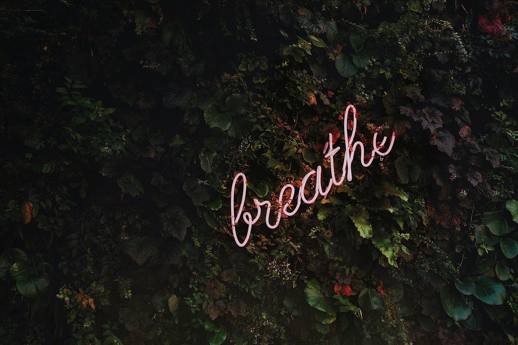 Leafy background with a neon sign saying breathe