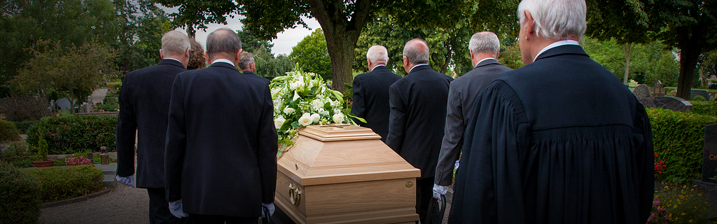 Pallbearers, all in dark suits, carrying a coffin.