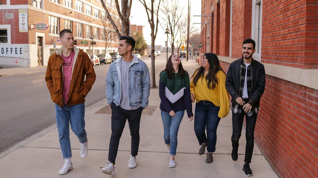 Five young adults, let’s say they’re students, walking along a pavement towards the camera