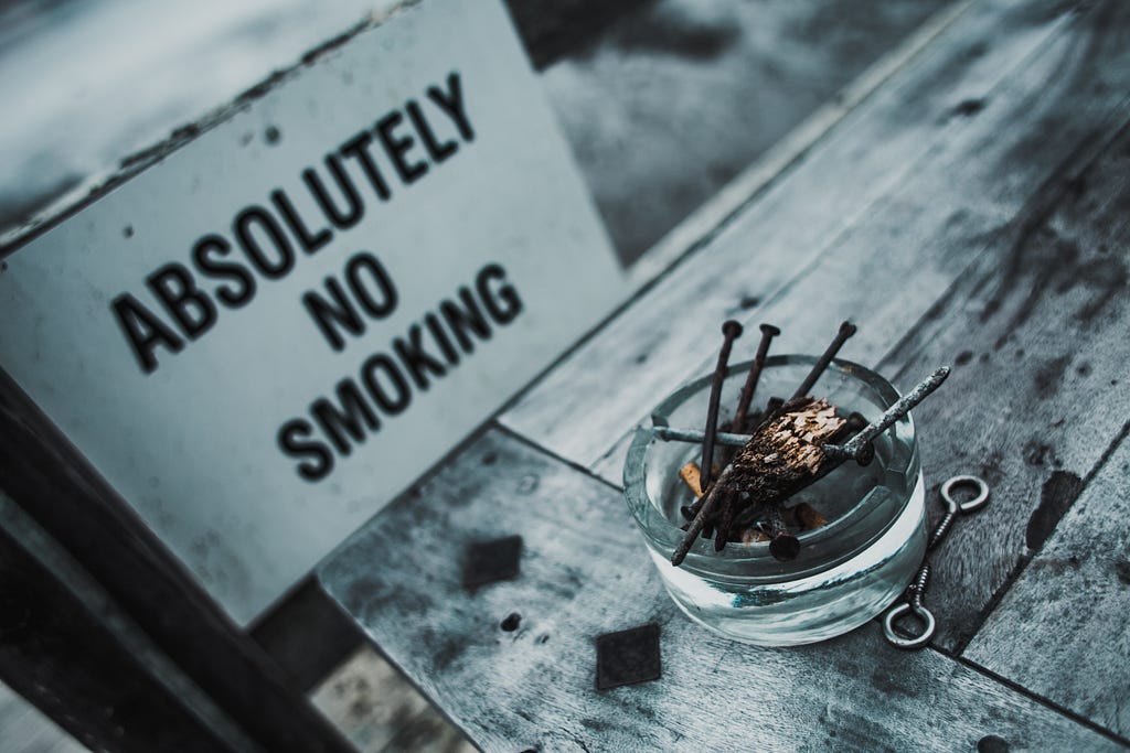 An-glass-ashtray-with-nails-balanced-on-it-and-an-extinguished-cigerette-and-a-board-written-with-absolutley-no-smoking-quit-smoking