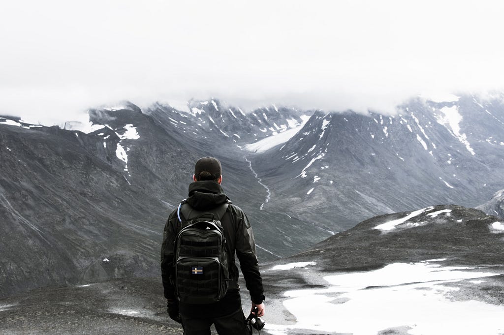 A man with a backpack, overlooking a snowy mountain area.