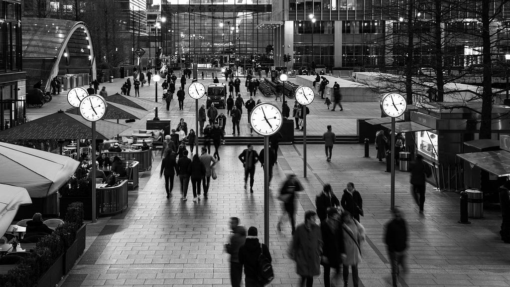 People walking in the street with many clocks around them