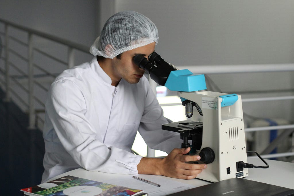 Researcher in lab, looking down microscope.