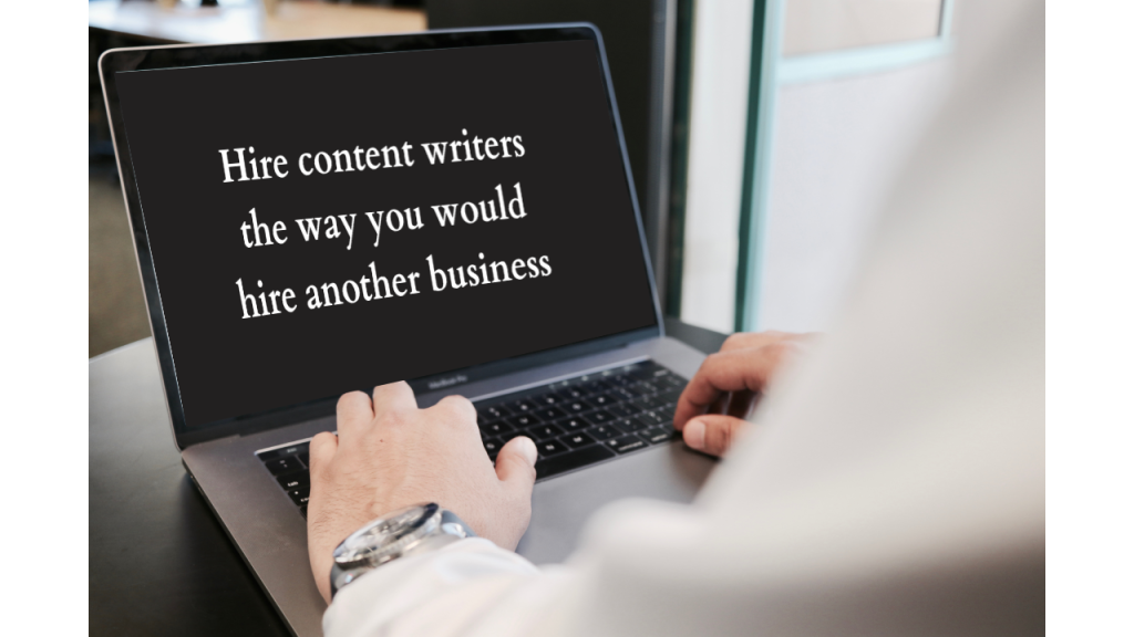 A person’s hands appears to be placed on a laptop’s keyboard with the screen reading the message “Hire content writers the way you would hire another business”