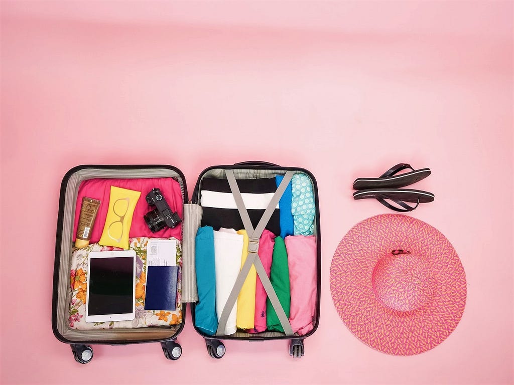 An open suitcase next to a hat and flip-flops.