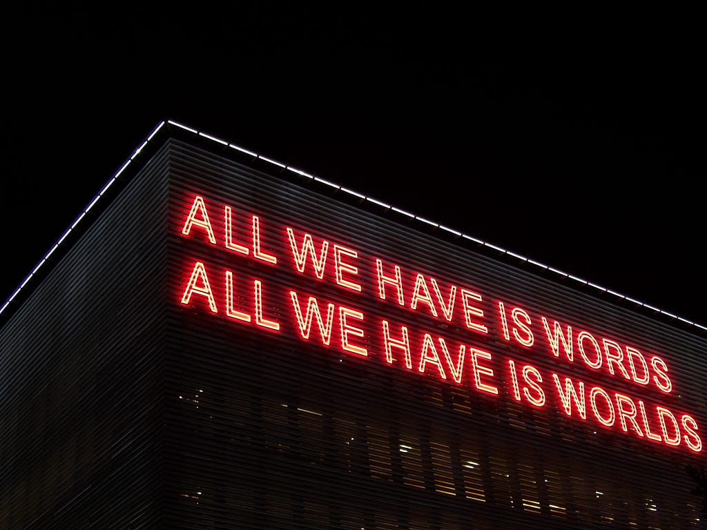 A neon sign saying “All we have is words, all we have is worlds”