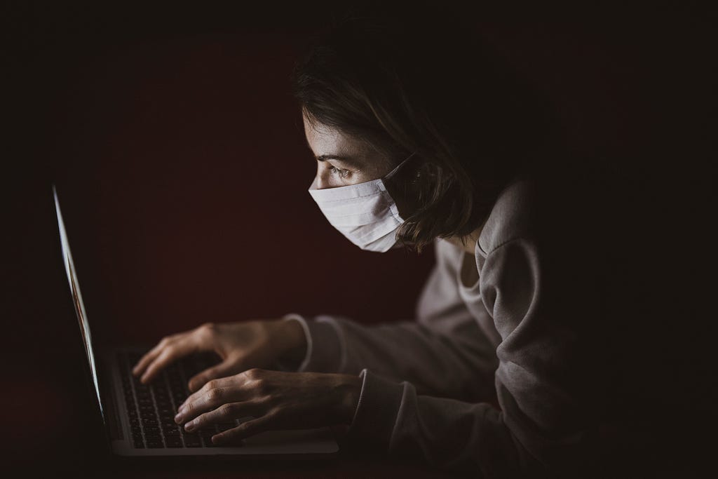 A women with a face mask checking her laptop in the dark.
