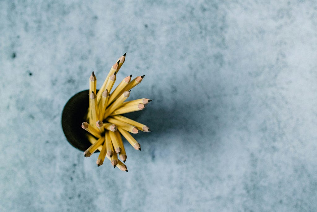 A birds eye view of a pencil pot filled with yellow pencils on a grey surface.