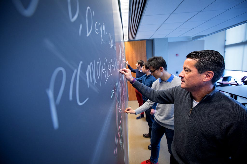 Four researchers write equations on a chalkboard.