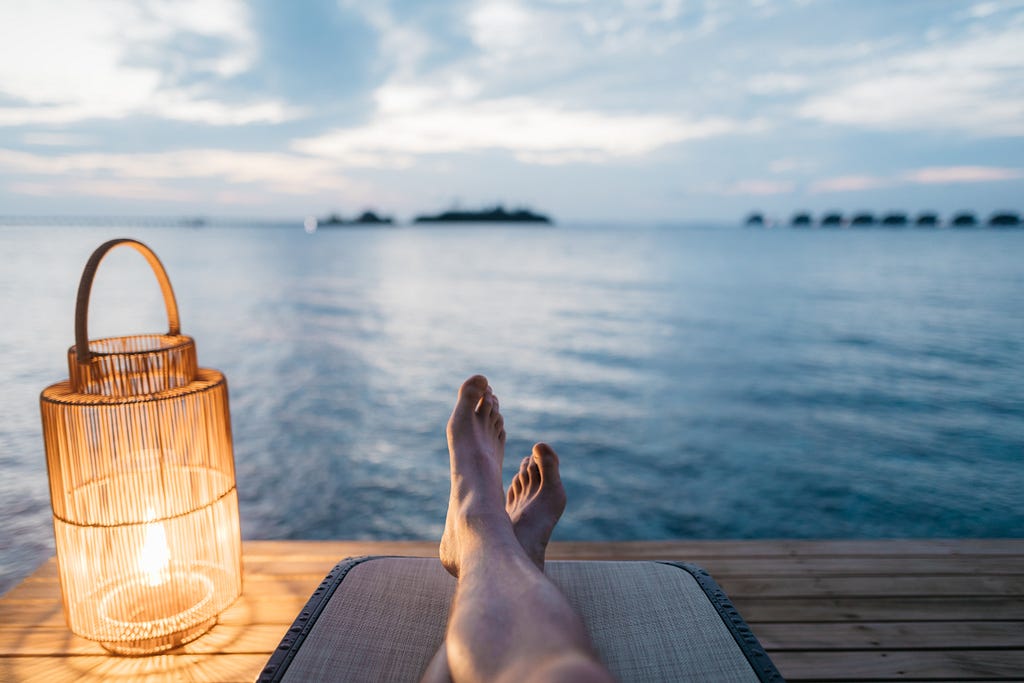 feet of a person relaxing on a dock overlooking an expanse of blue water