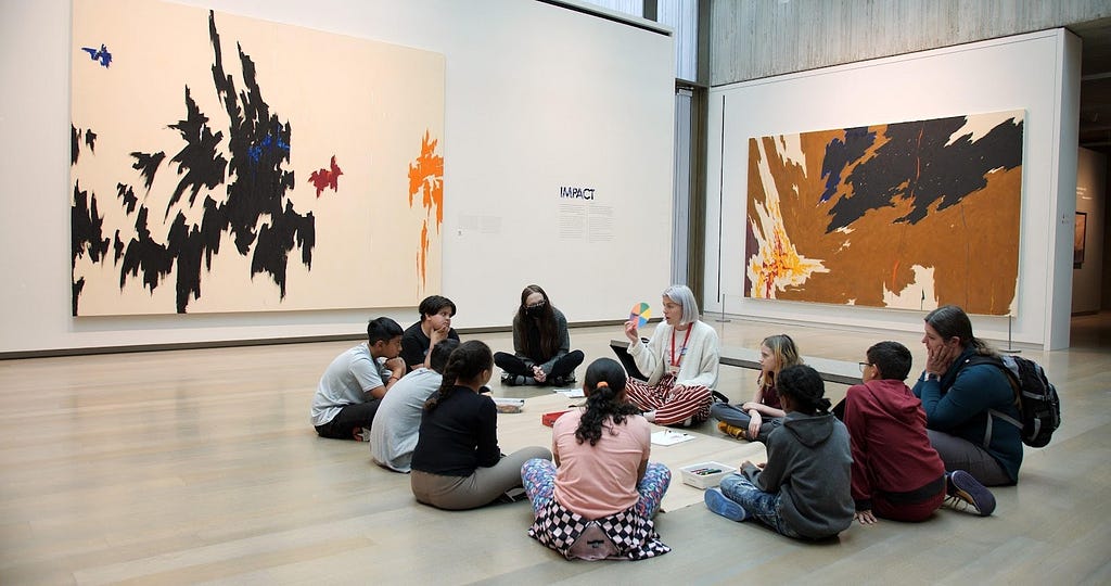 An educator and children sit in a circle on the floor in a gallery during an Instill lesson.