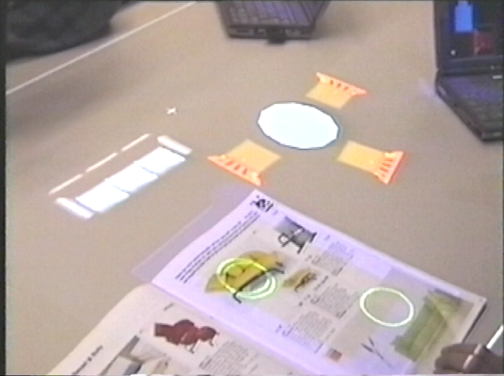 A catalog sits on a table with circled furniture; corresponding 3D models of the furniture are projected on the table.