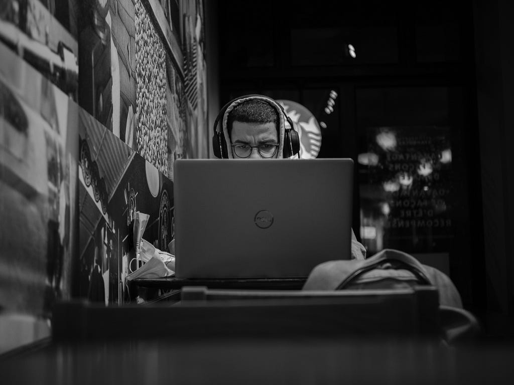 A person seated at a laptop in a coffee shop with large headphones on.