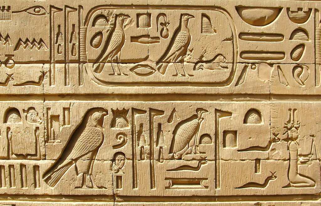 An area of a stone carving of ancient Egyptian hieroglyphs chiselled with great care and precision. The symbols shown are presented in two rows separated by a line. Some symbols are within a rounded-off box as if for emphasis.