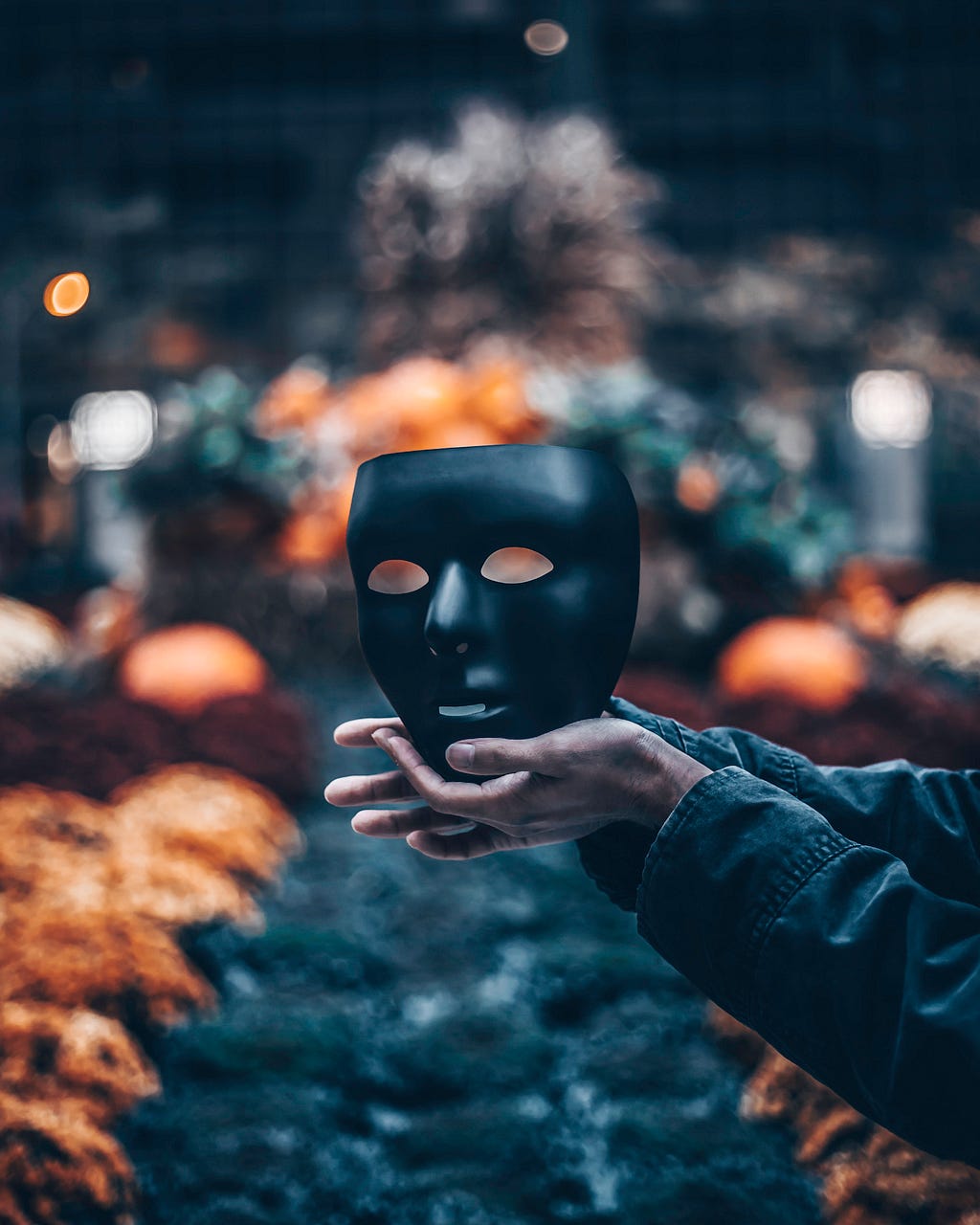 Picture of hands extended holding a black mask with blurred lights in the background