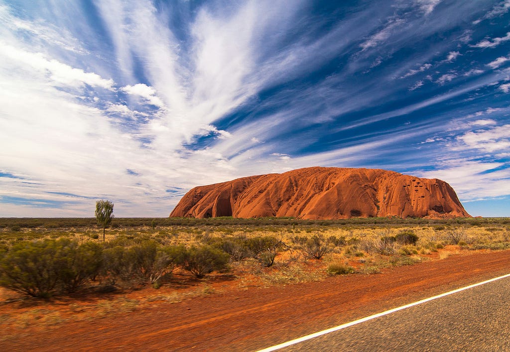 Australian Outback with giant red rock in backdrop.