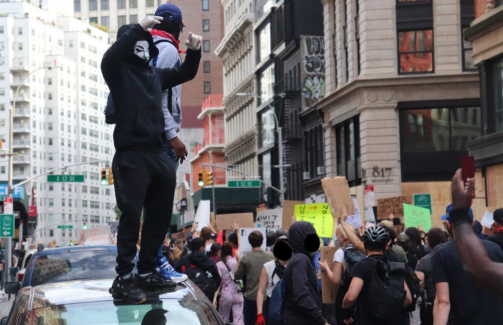 Two people stand on a car mere blocks away from Union Square, as rows of people next to them march in the streets.