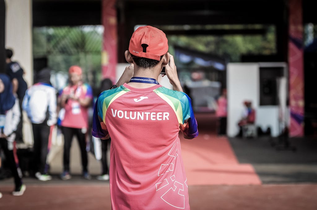 A man is photograghed from behind. His red sports top has “VOLUNTEER” in large white letters across his back.