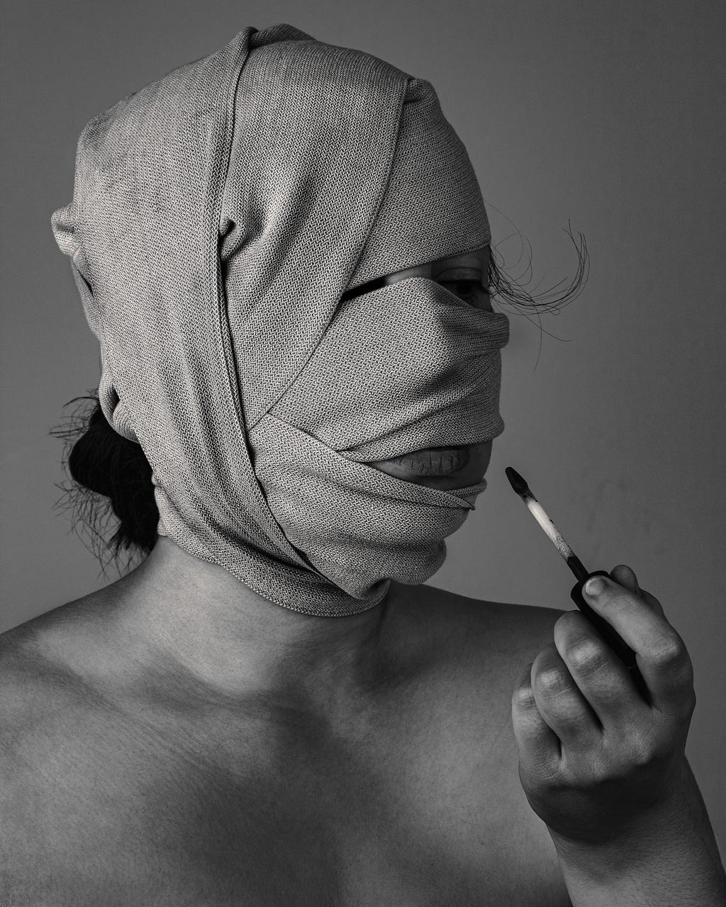 A woman with a cloth-wrapped head tries to carmine her lips.