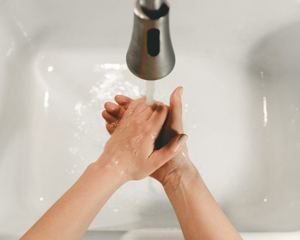 Two hands scrub beneath a faucet of flowing water