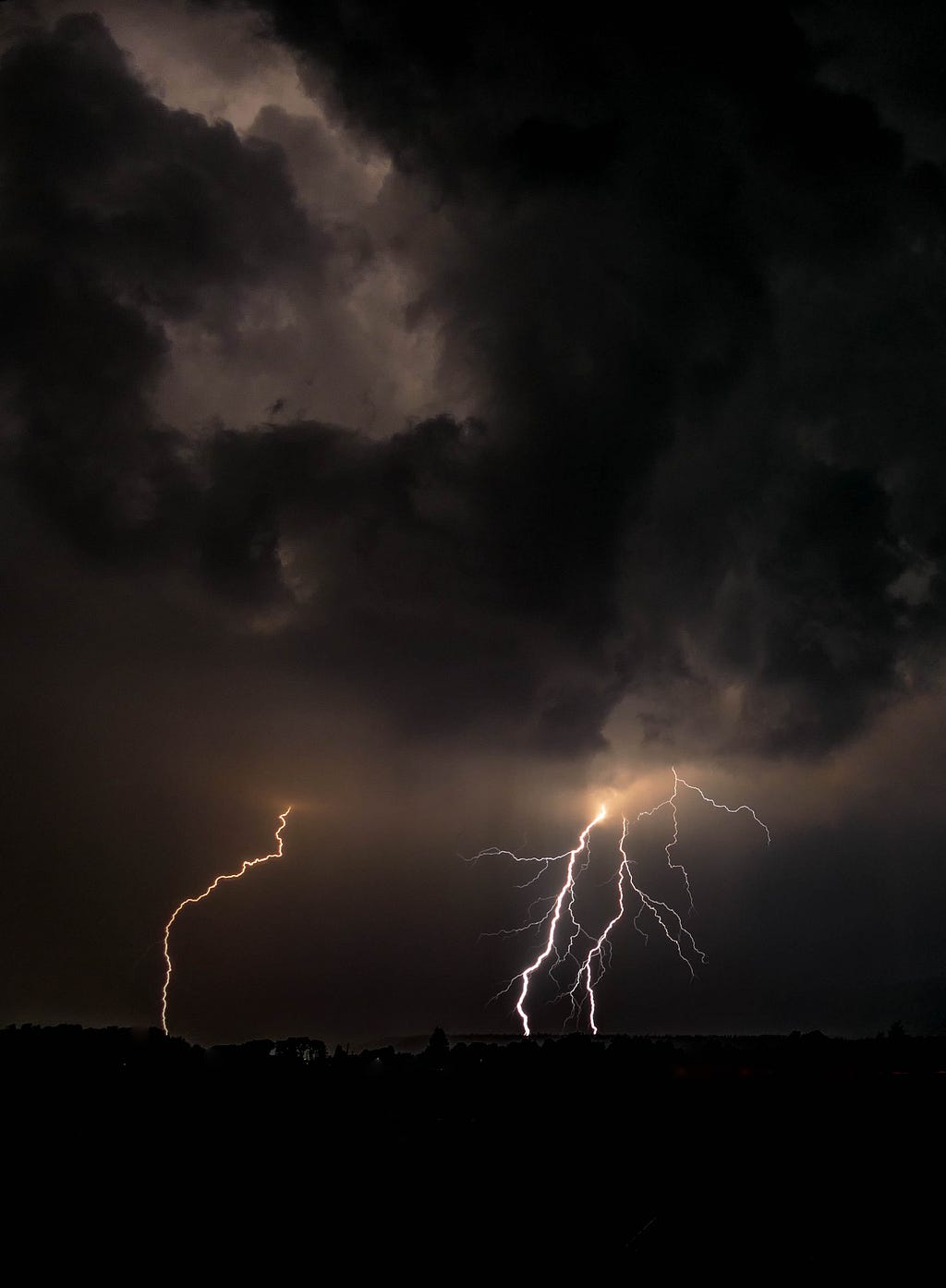 A dark and scary storm with multiple flashes of cloud-to-ground lightning.