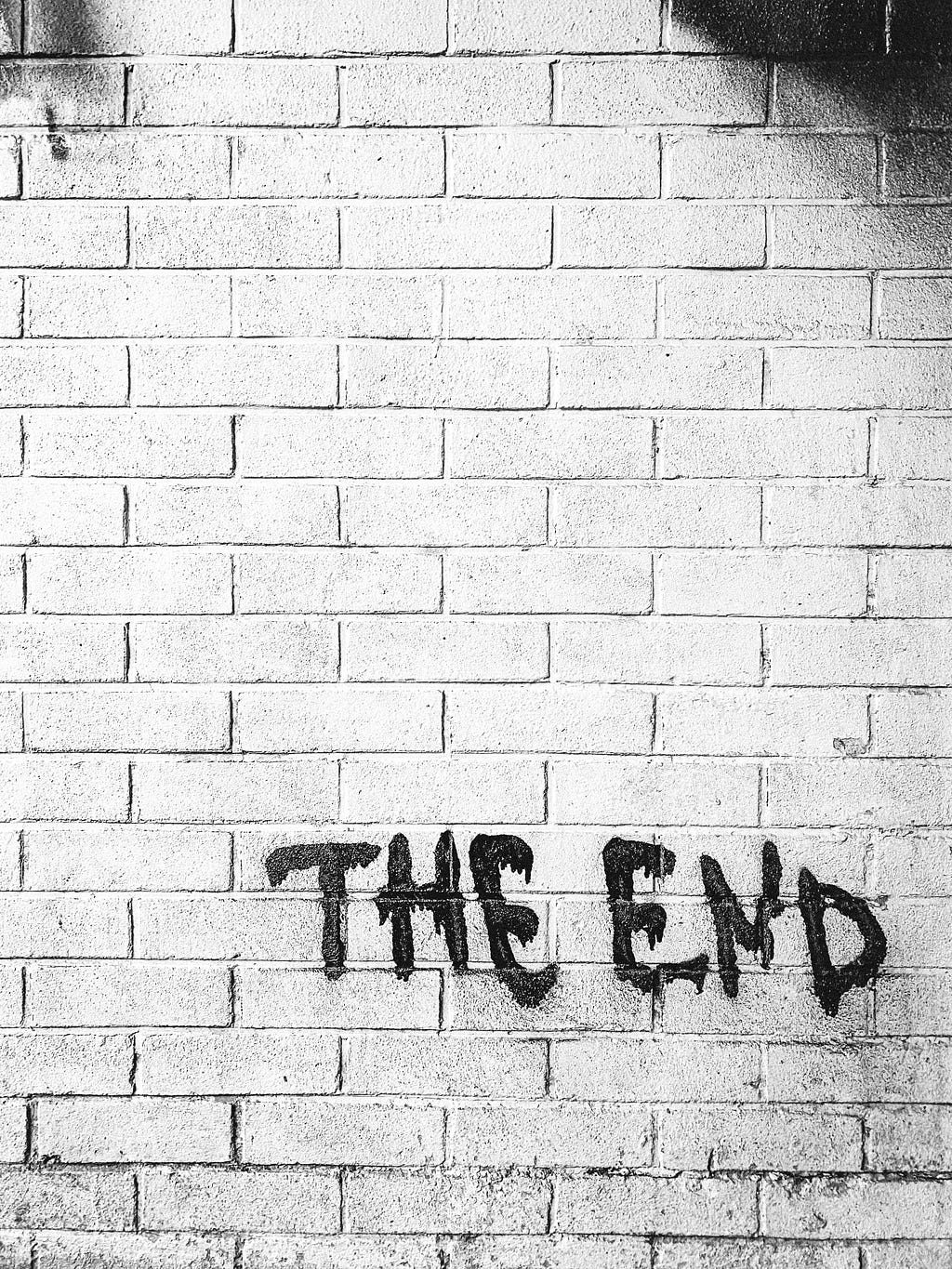 A black and white photo of a brick wall with “THE END” spraypainted on it