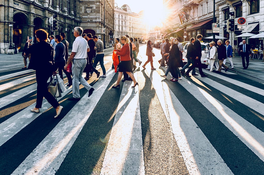 Pedestrians crossing a street in Vienna from different directions in the late afternoon as the sun begins to set.
