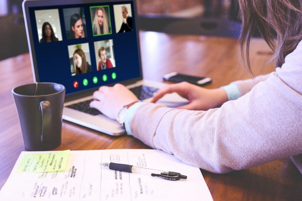 Photograph of a woman at a table using a laptop to take part in a video call, with a notebook in the foreground