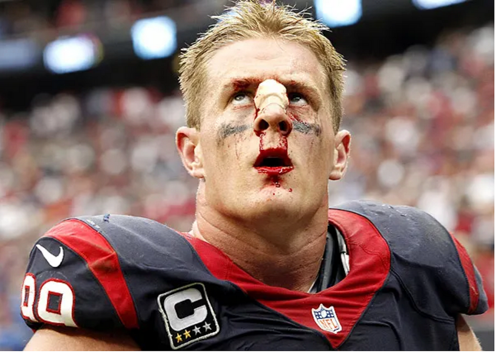 JJ Watt during a football match glaring up after suffering a nose injury evidenced by residual blood coming from his nose.