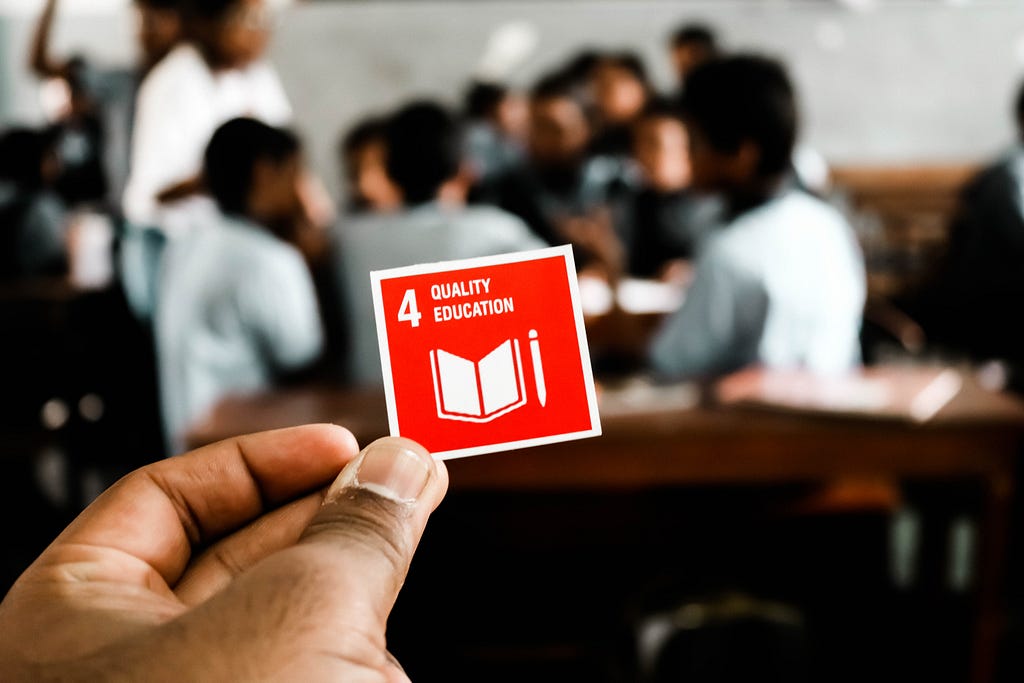 A hand holds out a card with the 4th sustainability goal: 4 Quality Education