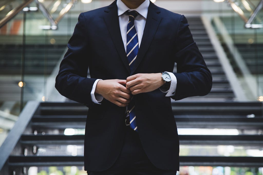 A body shot of a man wearing a suit standing at a stairway of an office building.