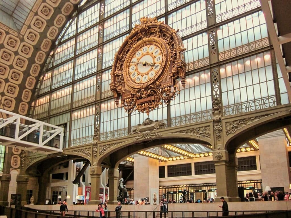 A large clock hangs from the ceiling of a large building.