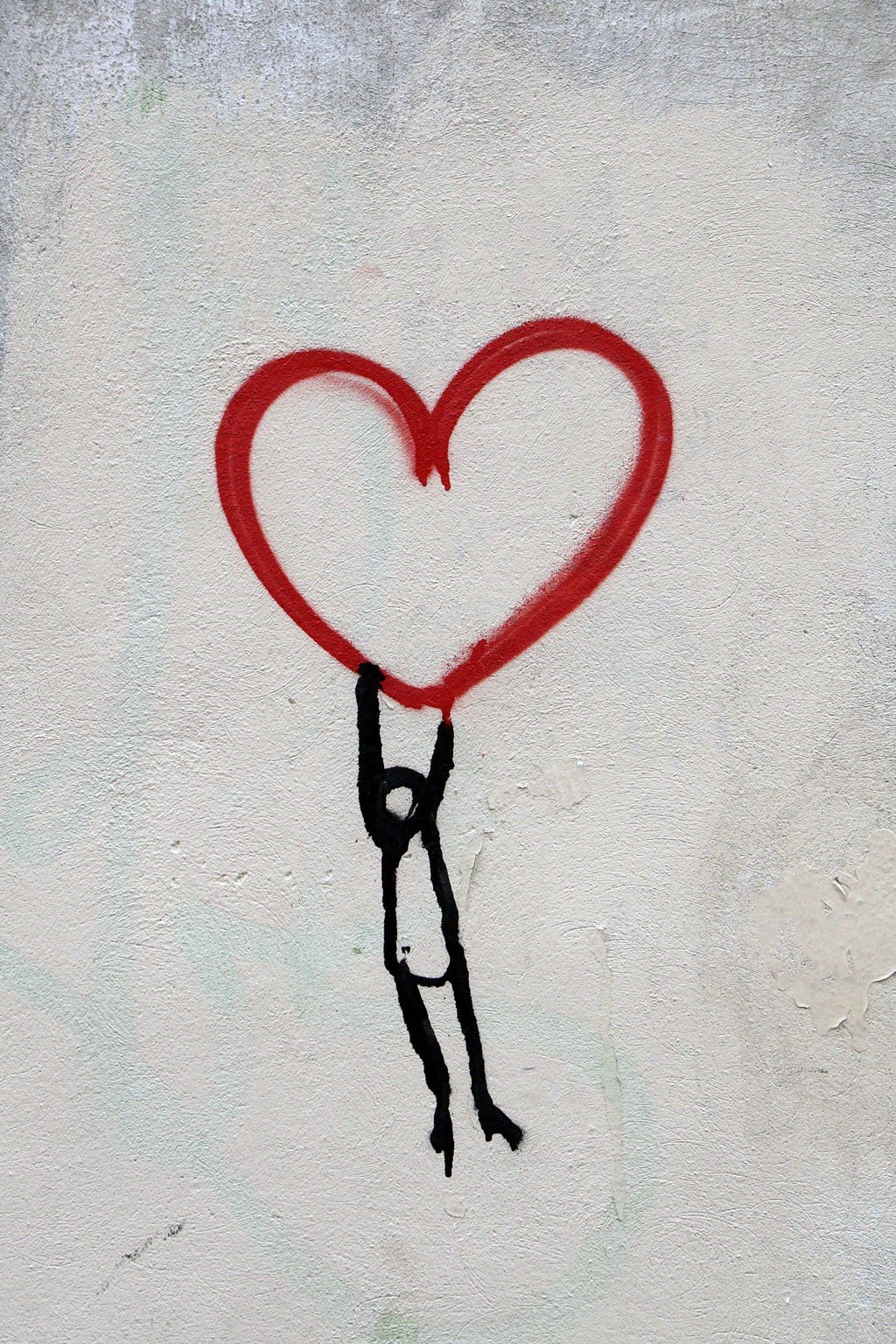An outline of a big heart in red, that seems to hang from a whitewashed wall, with an outline of a person, head bowed, hanging from its lowest point.