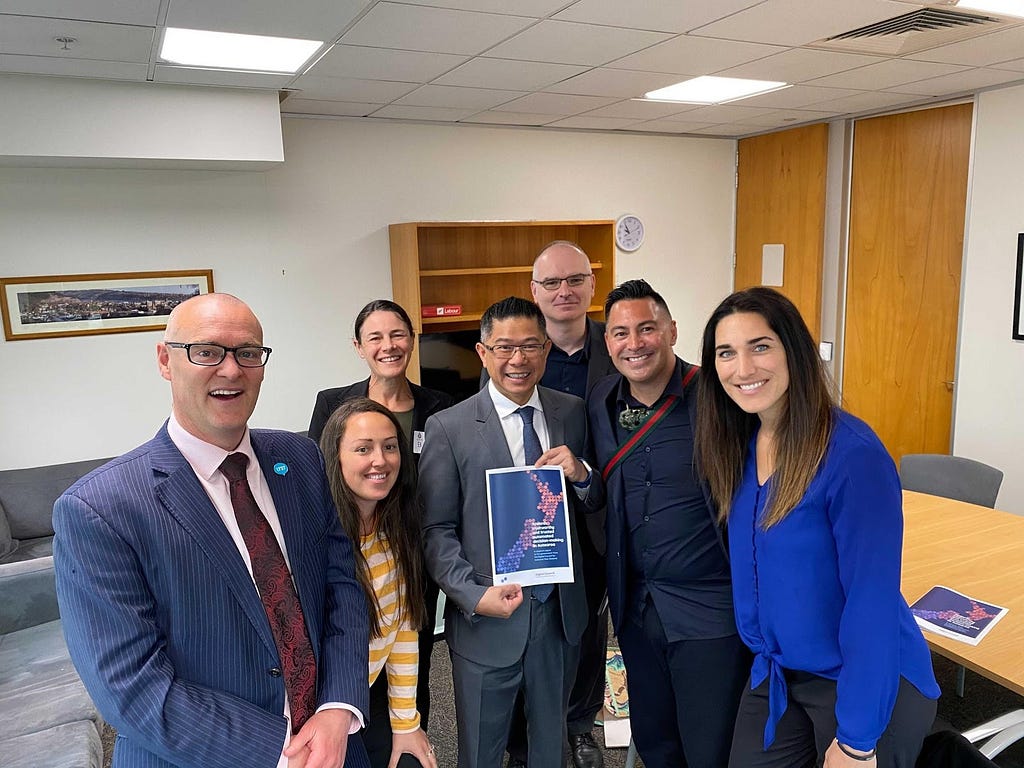 The Minister and Council members grouped together smiling at the camera. Mitchell Pham in centre holds a copy of the report.