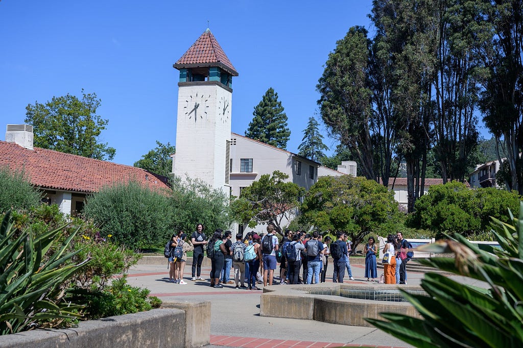 A large group of students gathered outside a dorm building with a clock tower in the background.