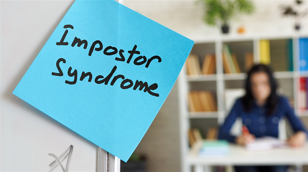 Blue sticky note with the words “Impostor Syndrome” written on it