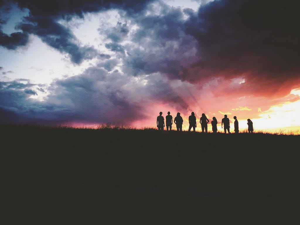 A group of people on a hill in silhouette, standing under a dramatic sunset.