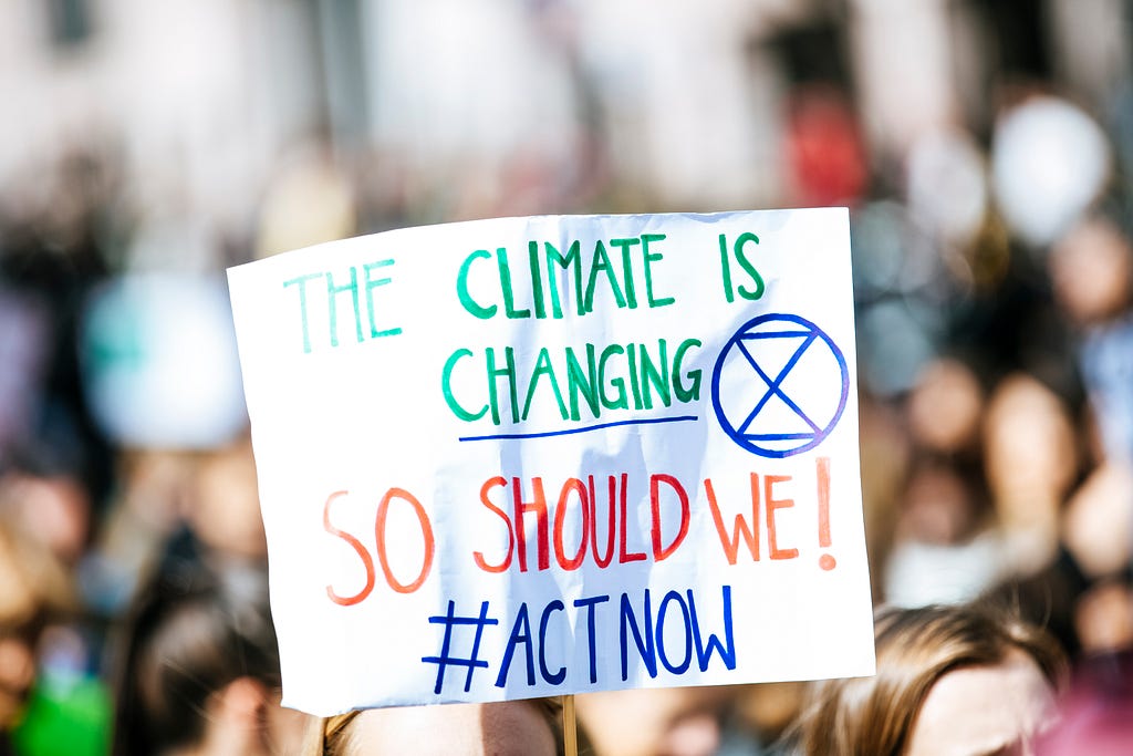 A protester holds up a white poster stating “The Climate is Changing, So Should We! #ACTNOW”