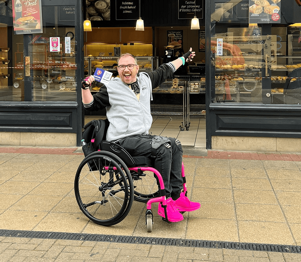 Damian in his wheelchair smiling with Sociability leaflet