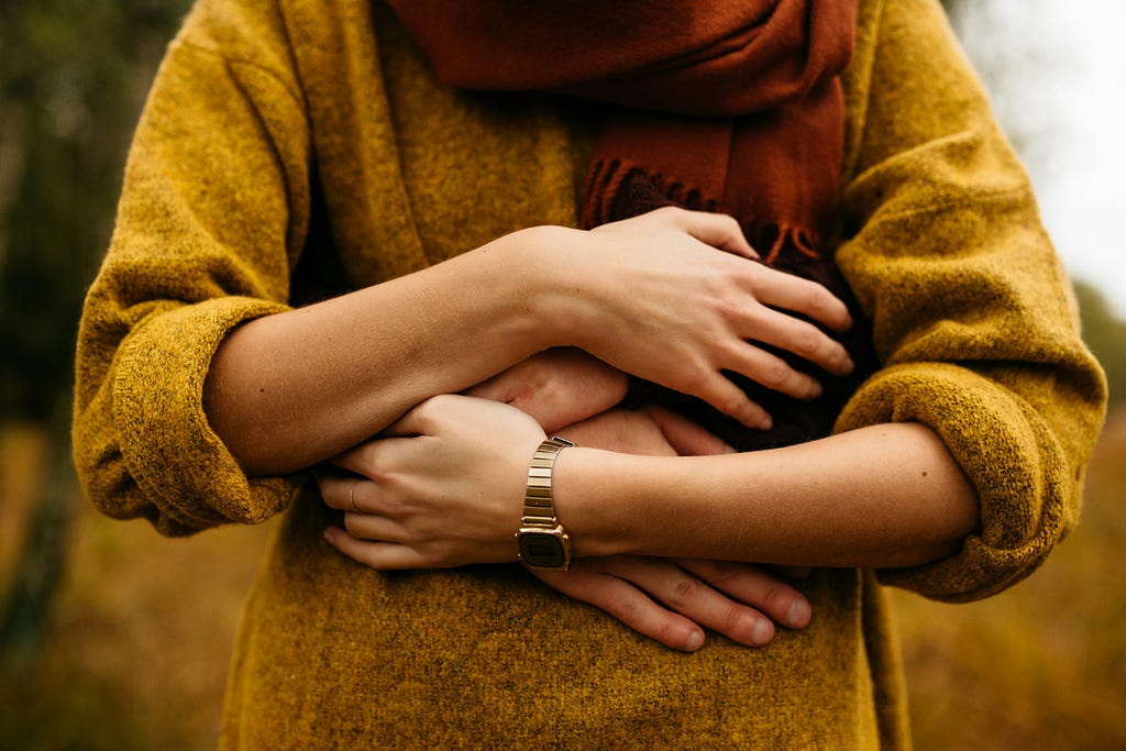 Woman in gold sweater twining arms with the person hugging her from behind.