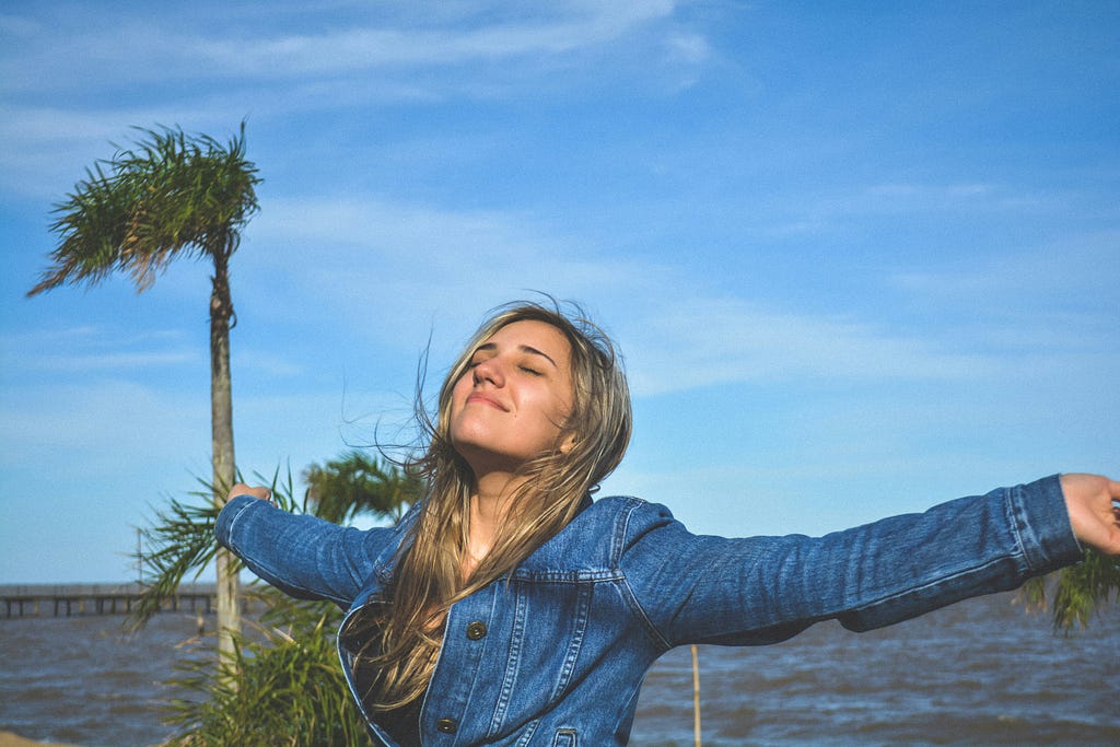 A girl closes her eyes and waves her hand in the air, taking a deep breath, expressing a sense of relaxation and calmness in solitude.