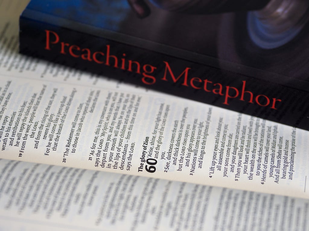 A closed book titled “Preaching Metaphor” lying on top of an open book.