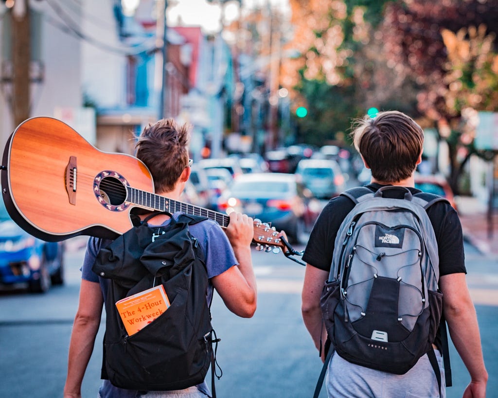 Digital Nomads walking through city with guitar and 4-hour work week book. // Photographer: Austin Distel | Source: Unsplash "www.distel.co". ❤️ 