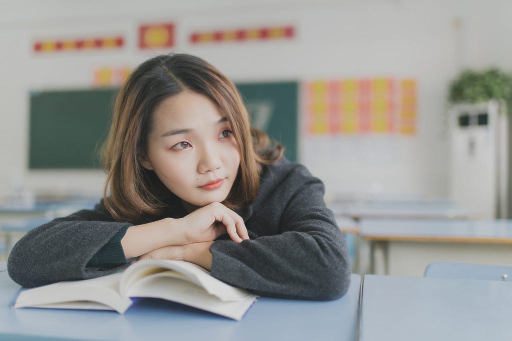 student leaning on her book and thinking about learning a language.