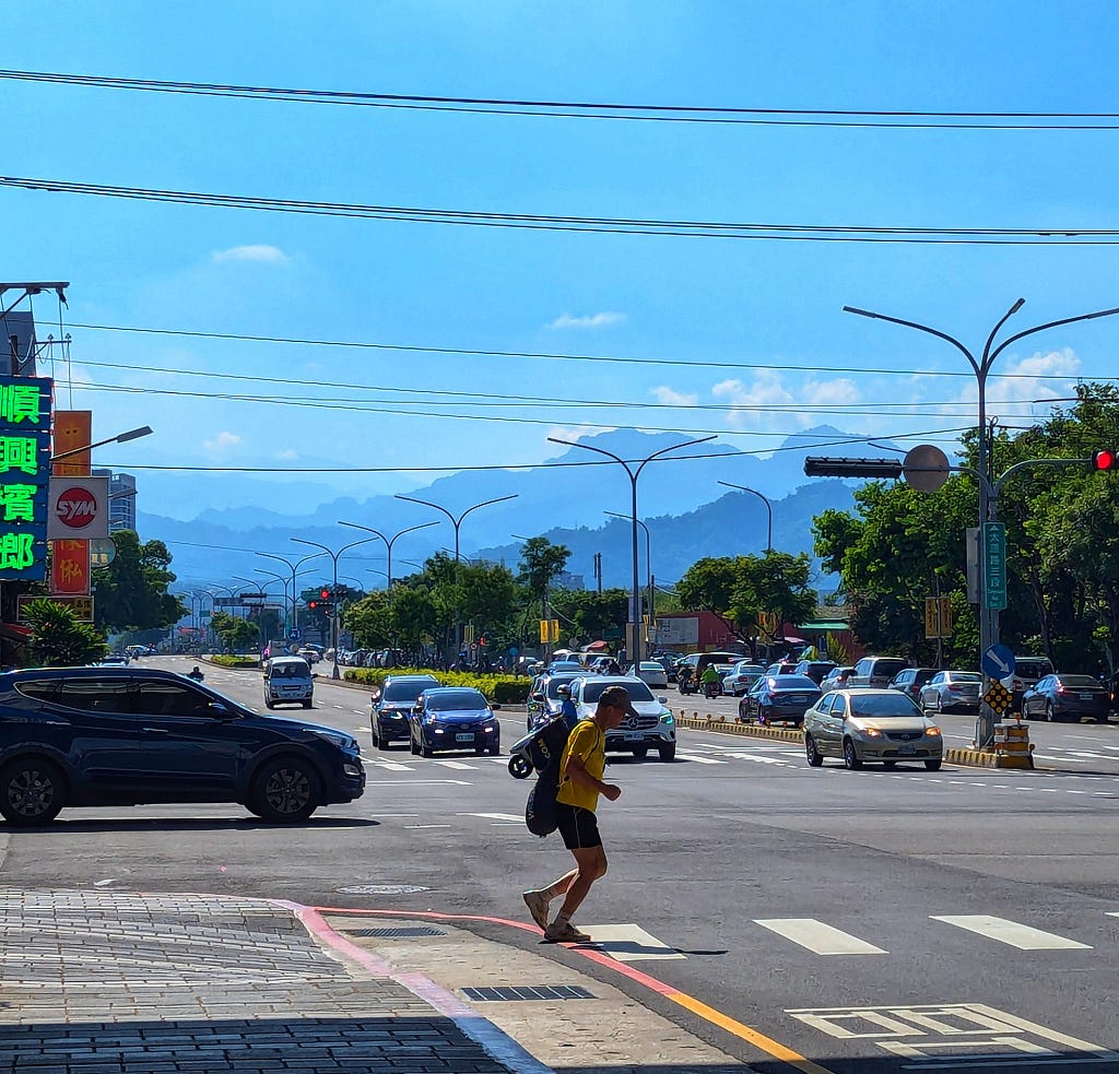 A man crossing the street with the Taichung mountains behind him.