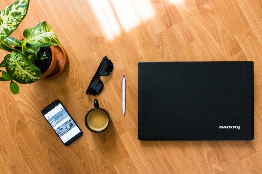 a lenovo laptop, smartphone, coffee mug and goggles on a table