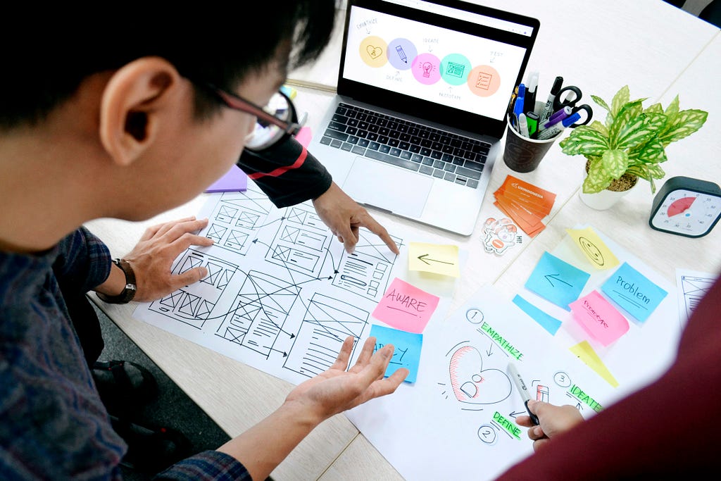 UX designers look at wireframes and colourful sticky notes on a table.