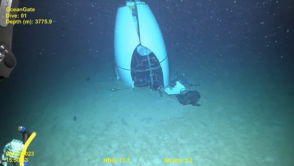 A still from the search for the wreckage of Titan. At the ocean floor, in a dark sandy desert, parts of the submersible are lying still.