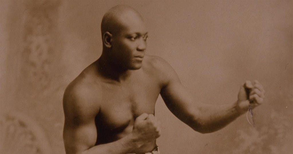 A man with a shaved head and brown skin stands in a boxing stance