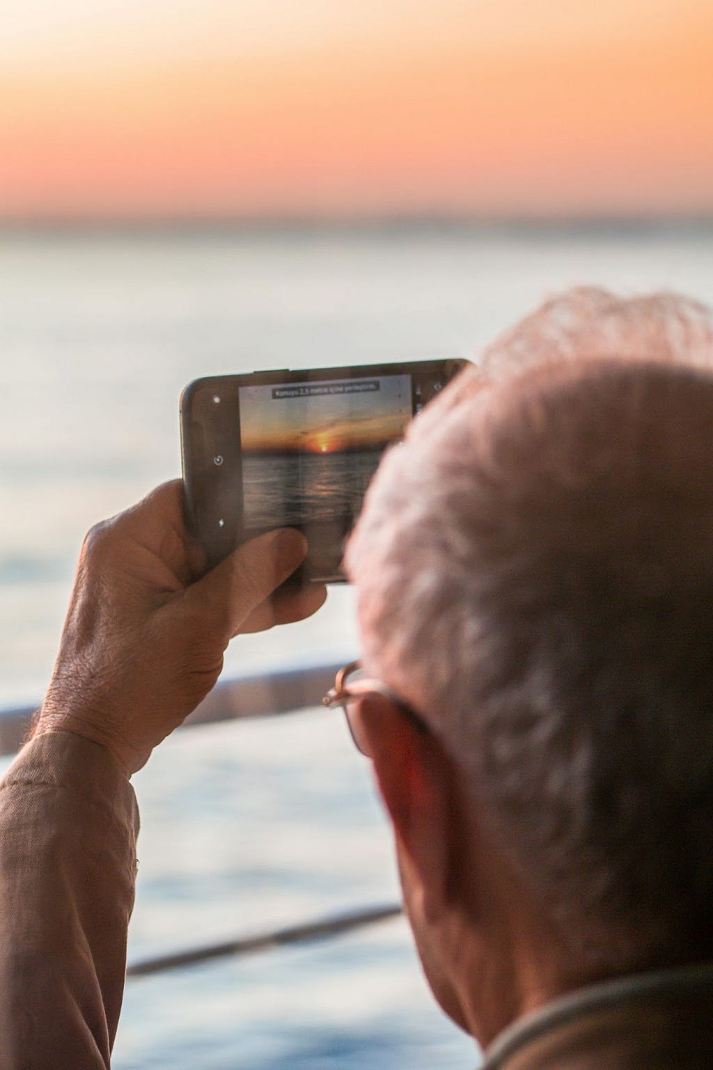 An elderly man taking a photo of the sunset on his smart phone
